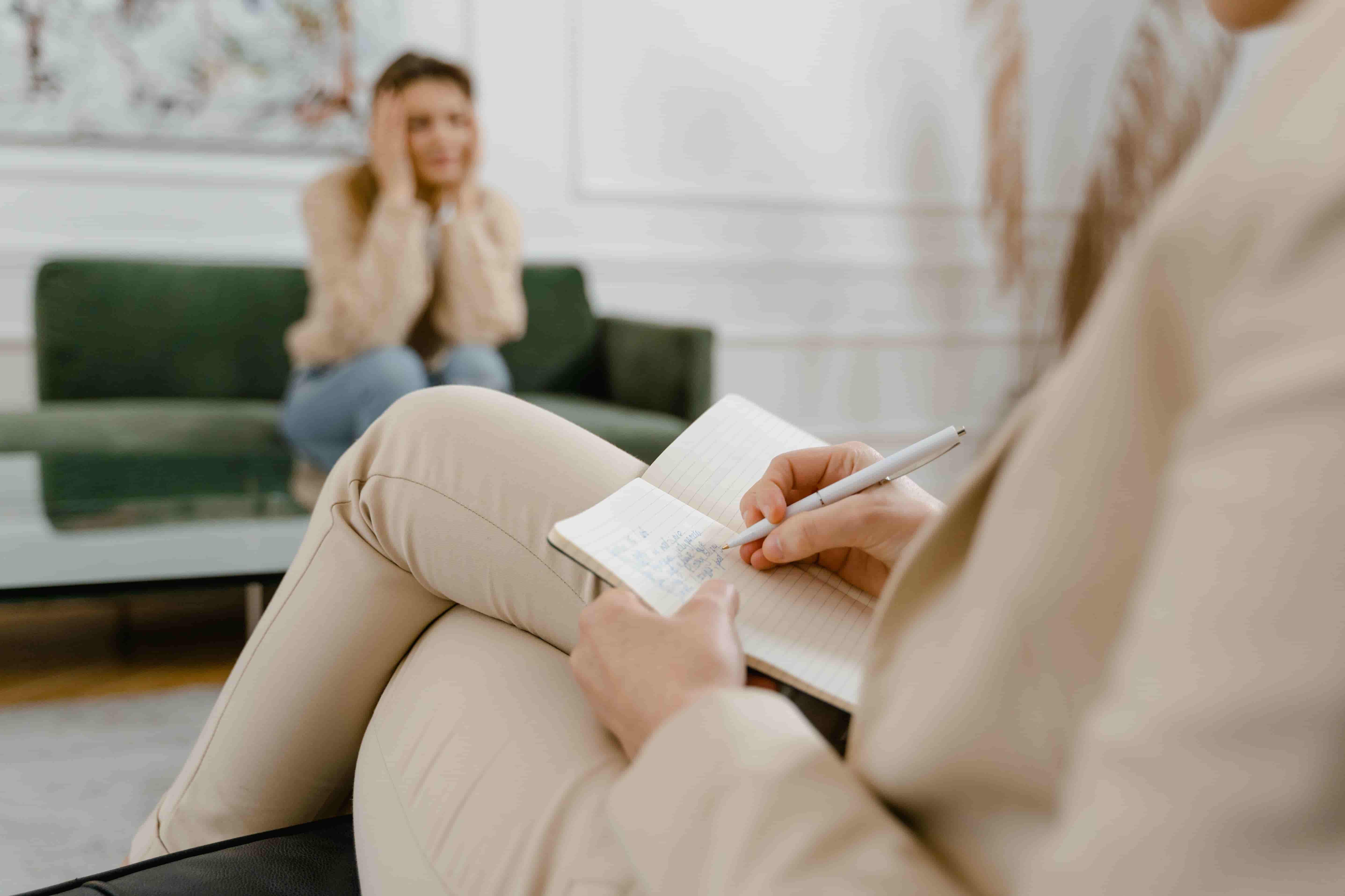 Therapeutin macht Notizen, im Hintergrund eine Klientin auf dem Sofa, ADHS-Diagnostik.