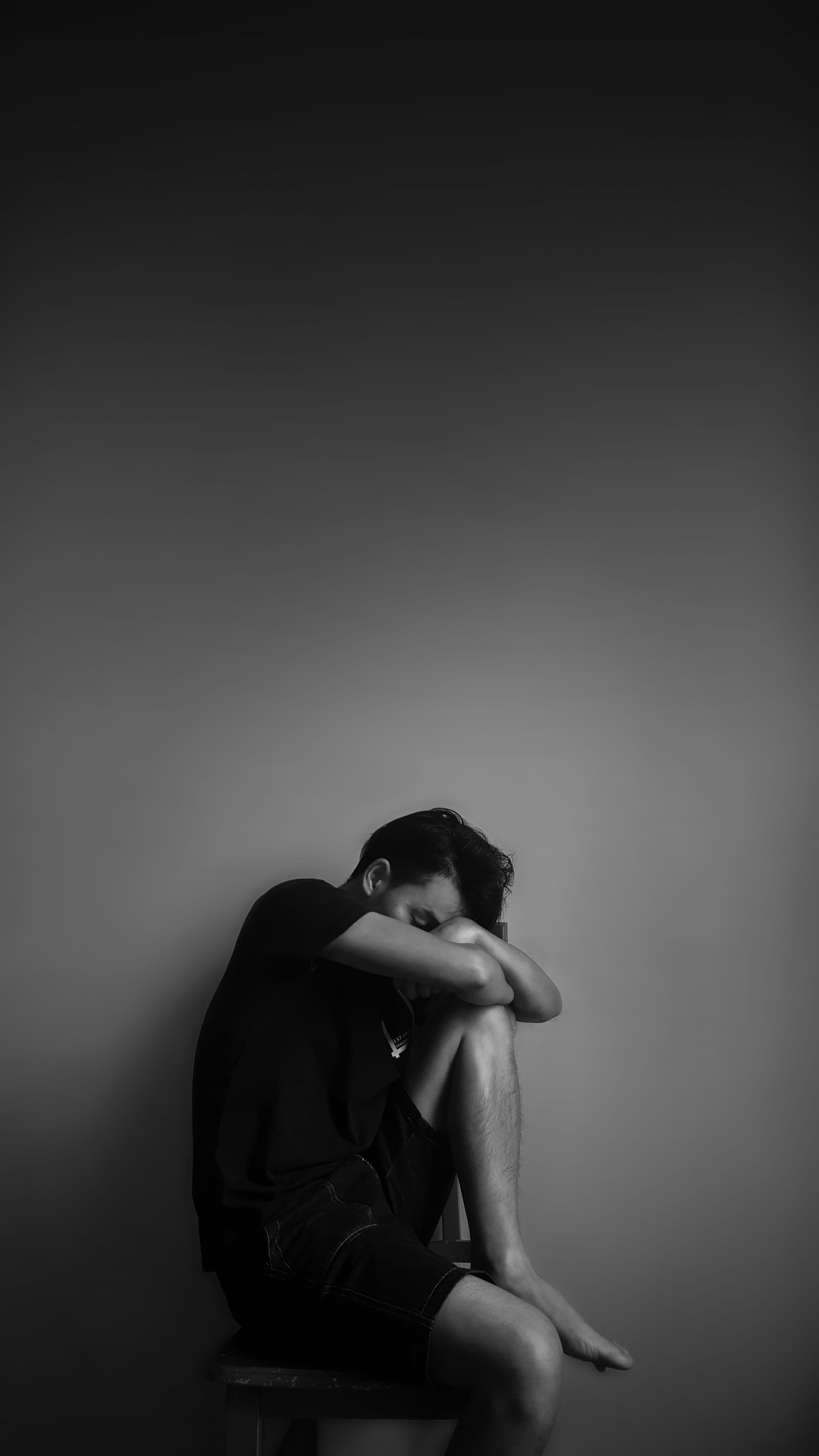 Person kauert allein an einer leeren Wand, den Kopf auf den Knien, Rückzug bei einer Depression.
