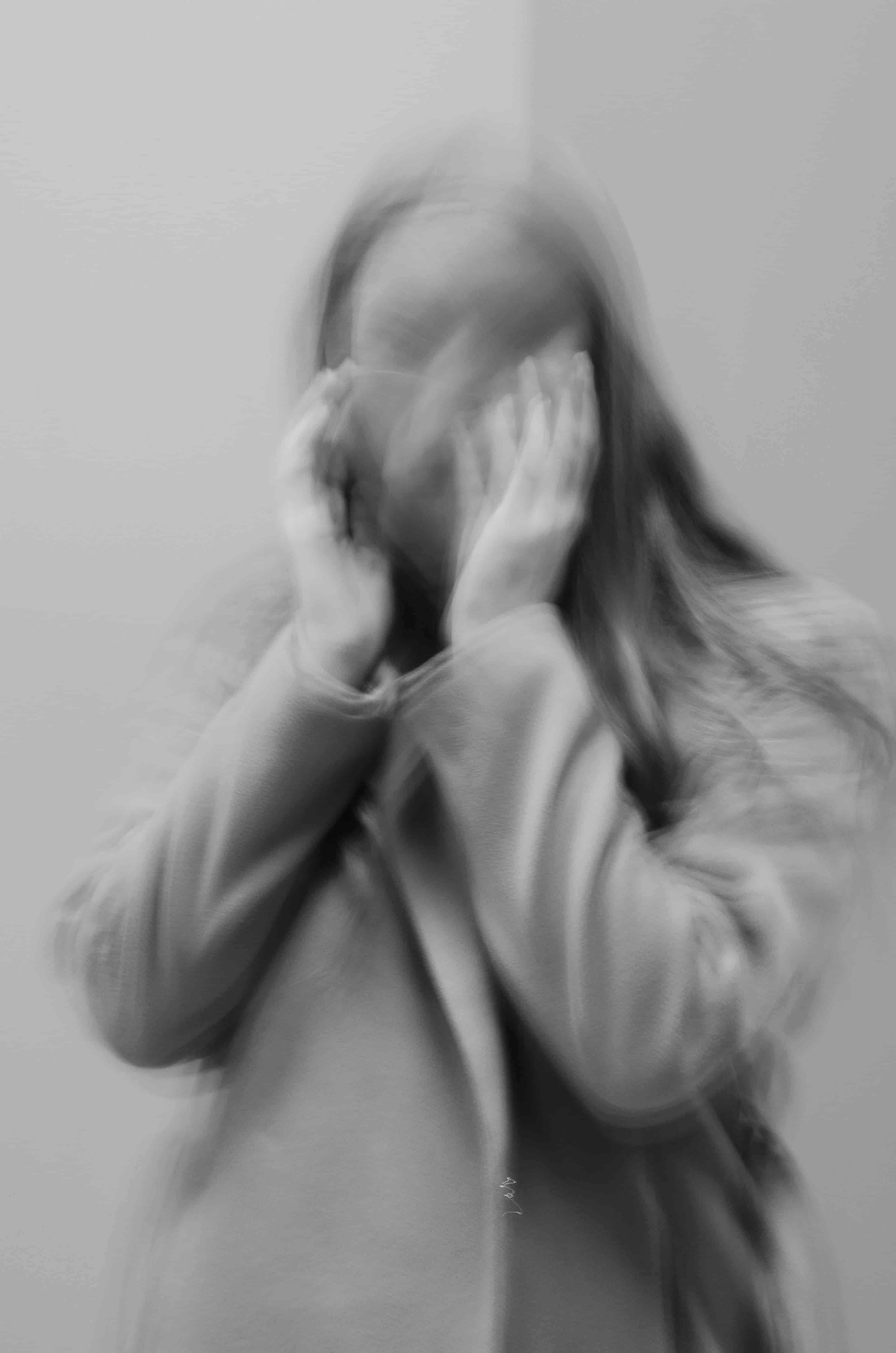 Bewegungsunscharfe Person mit den Händen am Kopf, Kontrollverlust während einer Panikattacke.