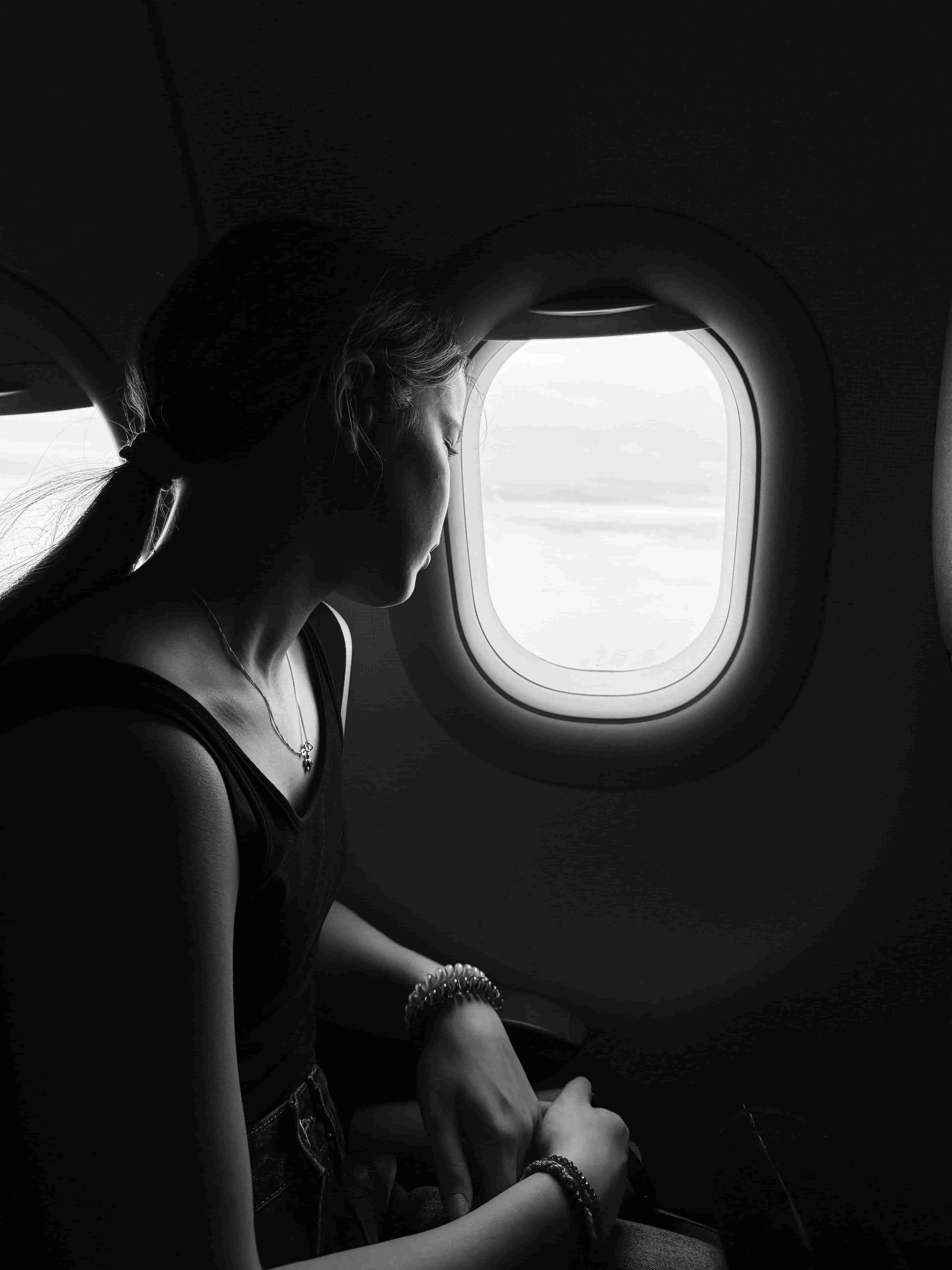 Junge Frau mit geschlossenen Augen angespannt am Flugzeugfenster, Flugangst als spezifische Phobie.