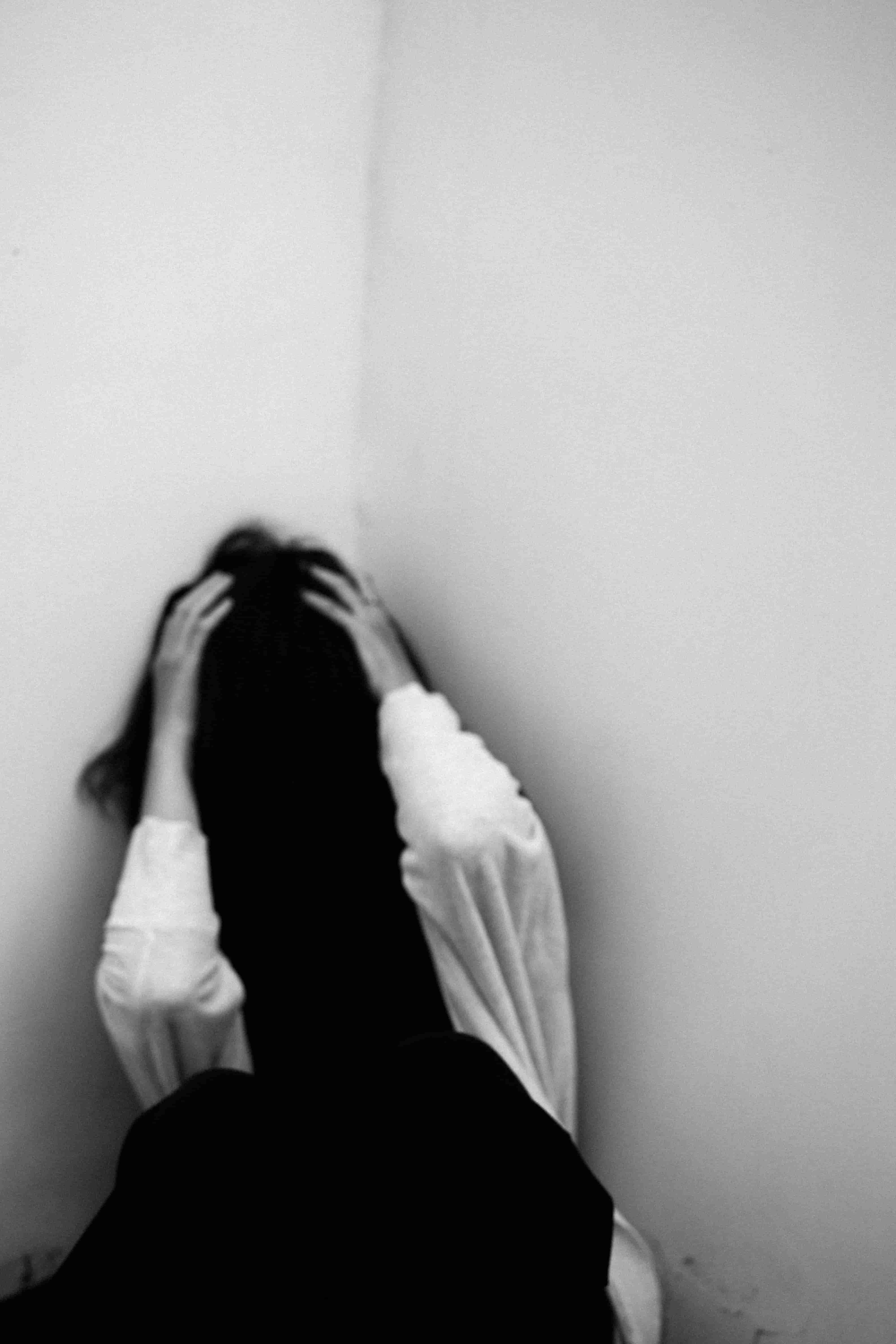 Person kauert in einer Zimmerecke und hält sich den Kopf, Belastung bei Trauma und PTBS.